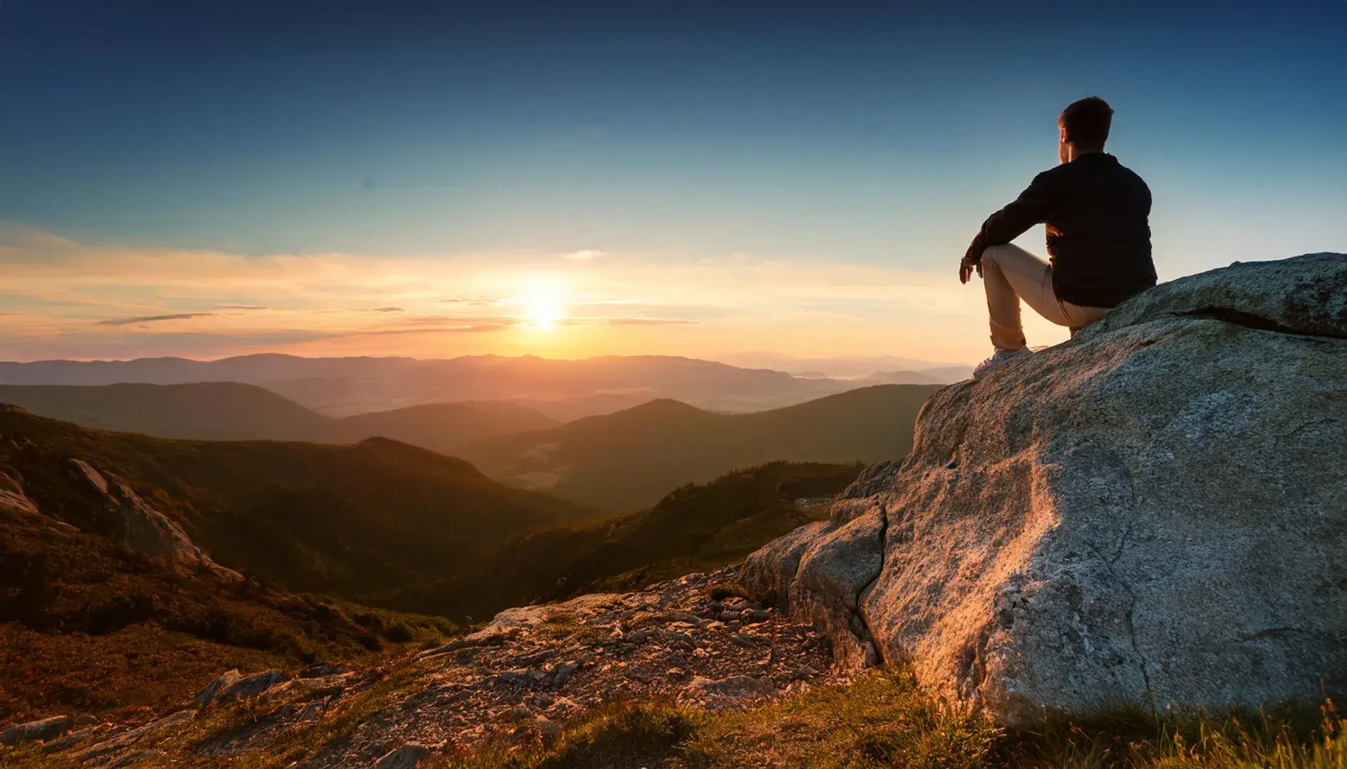 mensch sitzt auf einem Berg bei Sonnenuntergang und schaut in die beachtliche und traumhafte Ferne